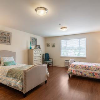 A spacious bedroom with two neatly made single beds, wooden flooring, and a large window allowing natural light.
