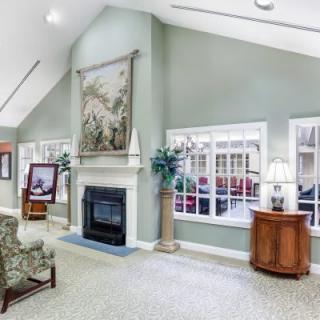 A spacious living room with a high ceiling, featuring a fireplace, decorative art, and ample natural light from large windows.