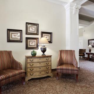 A classic living room with striped chairs, a wooden chest of drawers, and framed artwork on the wall.