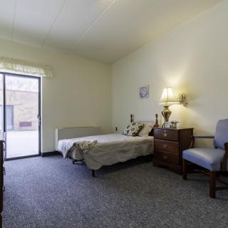 A minimalist bedroom with a bed, chair, and drawer under soft lighting.