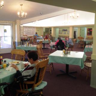 A cozy dining area with several people seated at tables covered with light blue tablecloths.