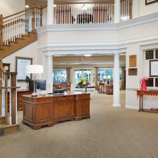 A spacious lobby with a wooden reception desk, staircase, and large columns.