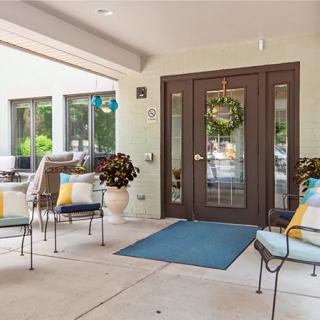 A cozy patio area with cushioned chairs, a decorative wreath on the front door, and potted plants creating an inviting atmosphere.