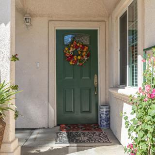 A welcoming green front door adorned with a colorful wreath, surrounded by potted plants.