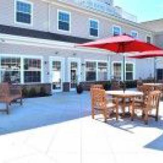 A sunny outdoor patio with tables, chairs, and red umbrellas in front of a building.