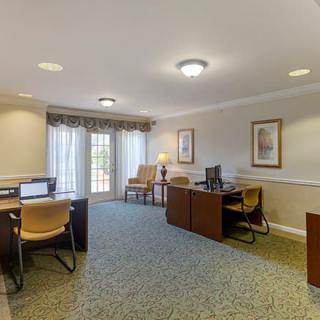 A well-lit office space featuring desks with computers, chairs, and large windows.