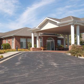 A residential building with a driveway and prominent entrance featuring columns.