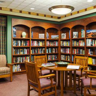 A cozy library corner with bookshelves, a round table, and comfortable chairs.