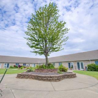 A tree stands in the center of a landscaped courtyard surrounded by buildings under a cloudy sky.