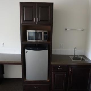 A compact kitchenette featuring a microwave, refrigerator, sink, and dark wood cabinets.