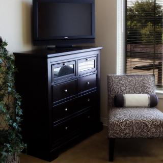 A cozy indoor setup with a television on a dresser and an upholstered chair by the window.