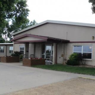 Entrance of a single-story building with a driveway and surrounding trees.