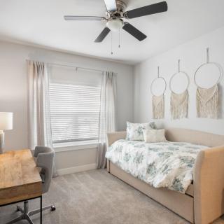 A cozy bedroom featuring a daybed, desk, and ceiling fan with soft lighting and subtle wall decor.