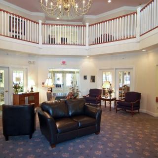 A spacious lobby with elegant furniture and a central chandelier, featuring a second-floor balcony overlooking the area.