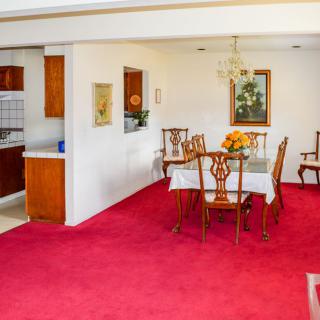 A dining room with red carpeting and wooden furniture, featuring a table with chairs and a chandelier overhead.