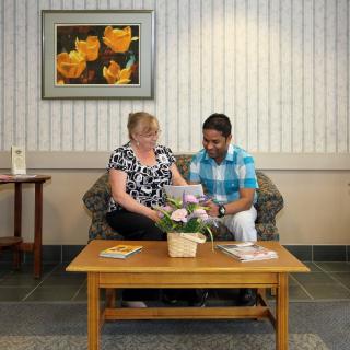Two people sitting in a waiting room, engaging in conversation while looking at documents.