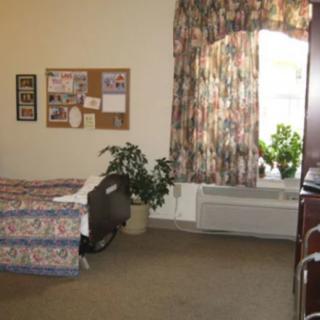 A cozy bedroom with floral curtains, a bed, plants, and a bulletin board on the wall.