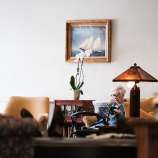 An elderly person reading in a cozy living room with warm lighting and tasteful decor.