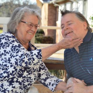 An elderly woman playfully interacting with a man outdoors, both smiling.