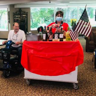 A festive indoor setup with beverages and American flags, featuring a person wearing a mask and another seated nearby.