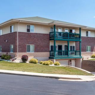 A modern two-story apartment building with brick exterior and balconies, surrounded by landscaped greenery.