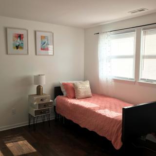 A minimalist bedroom with a single bed, pink bedding, and natural light streaming through the window.