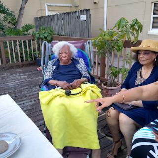 A heartfelt family gathering outdoors, featuring an elderly woman in a wheelchair surrounded by loved ones.
