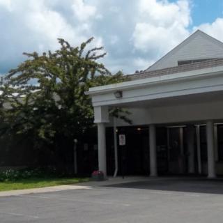 A building entrance with a covered entryway and trees nearby under a cloudy sky.