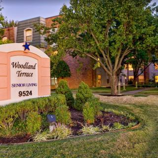 Entrance sign for Woodland Terrace apartment complex surrounded by lush landscaping.