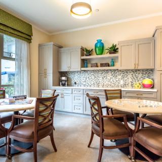 A bright kitchen and dining area with wooden chairs, a round table, and stylish cabinetry accented by a colorful mosaic backsplash.