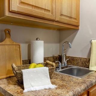 A neat kitchen countertop with a sink, wooden cabinets, and a fruit basket.