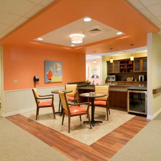 A modern dining area with orange walls and a small kitchenette.