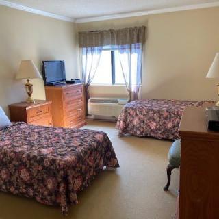 A hotel room with two single beds, a television on a dresser, and a window.