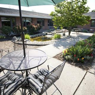 A serene patio area with a metal table, chairs, and an umbrella, surrounded by a lush garden.