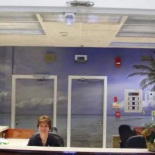 A person sitting at a reception desk with a beach-themed mural in the background.