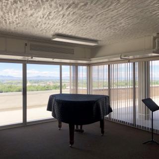 A room with large windows showcasing a mountain view, featuring a covered grand piano and a music stand.