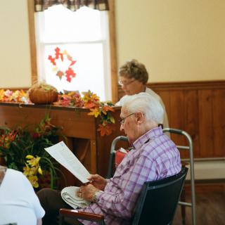 Elderly individuals engaged in reading during a community gathering with autumn-themed decorations.