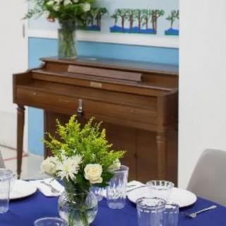 A dining table set with elegant decor next to a wooden piano.