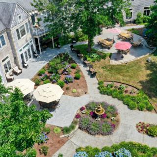 Aerial view of a landscaped garden with pathways, patio areas, and umbrellas near a building.