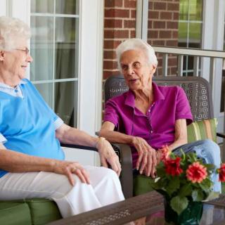 Two elderly women enjoying a conversation on a porch.