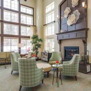 A cozy living room with large windows, armchairs around a round table, and a fireplace adorned with floral decorations.