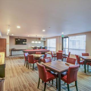 A modern dining area with red chairs and wooden tables, featuring a mounted television and warm lighting.