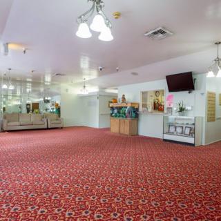 A spacious lobby area featuring red carpet, comfortable seating, mirrors, and a wall-mounted television.