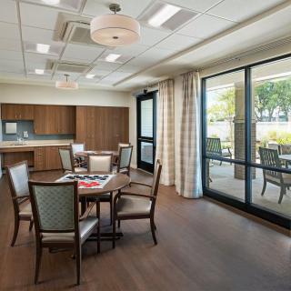 A modern dining room with a set of tables and chairs, featuring large windows with curtains and wood flooring.