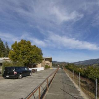 A scenic outdoor pathway with a car parked beside trees and a building under a partly cloudy sky.