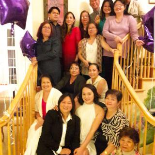 A group of people gathered on a staircase for a family event, surrounded by purple balloons.