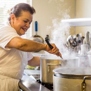 A woman cooking in a kitchen, stirring a pot on the stove with steam rising.