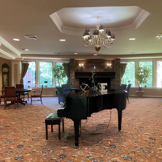 An elegant music room featuring a grand piano and chandelier, with large windows providing natural light.