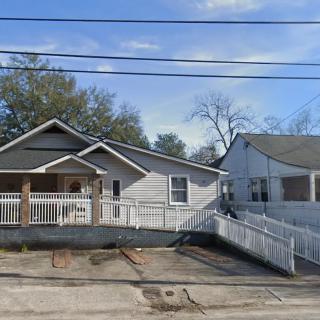 A residential house with a ramp and fence in front, situated on a driveway under a clear sky.
