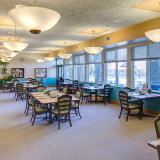 A spacious dining room with several tables and chairs arranged neatly, featuring large windows and elegant lighting fixtures.